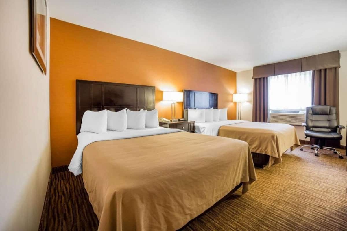Habitación de hotel con dos camas, un escritorio, una silla y un ventanal con cortinas.