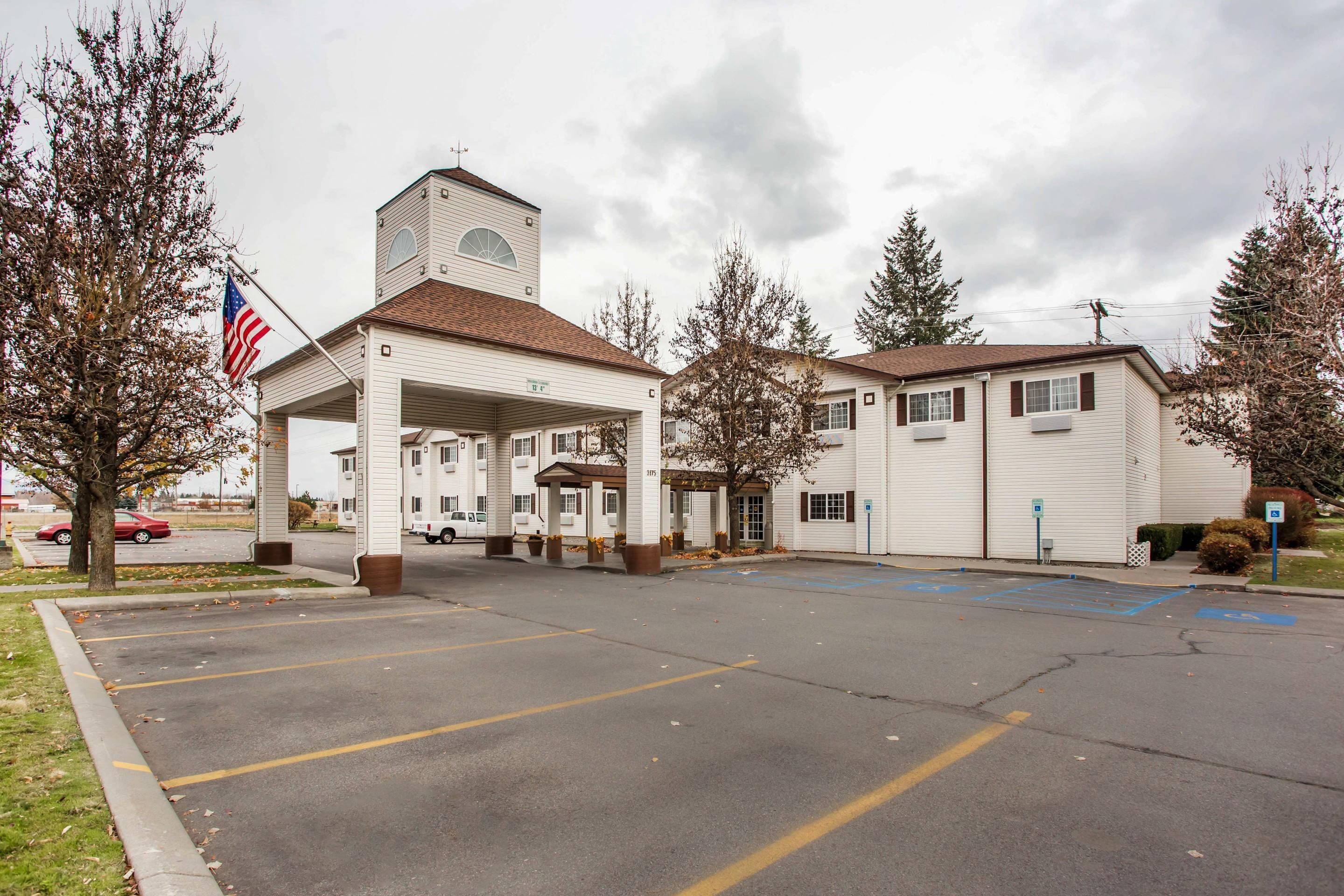 Un motel con edificio central, estacionamiento y una bandera.