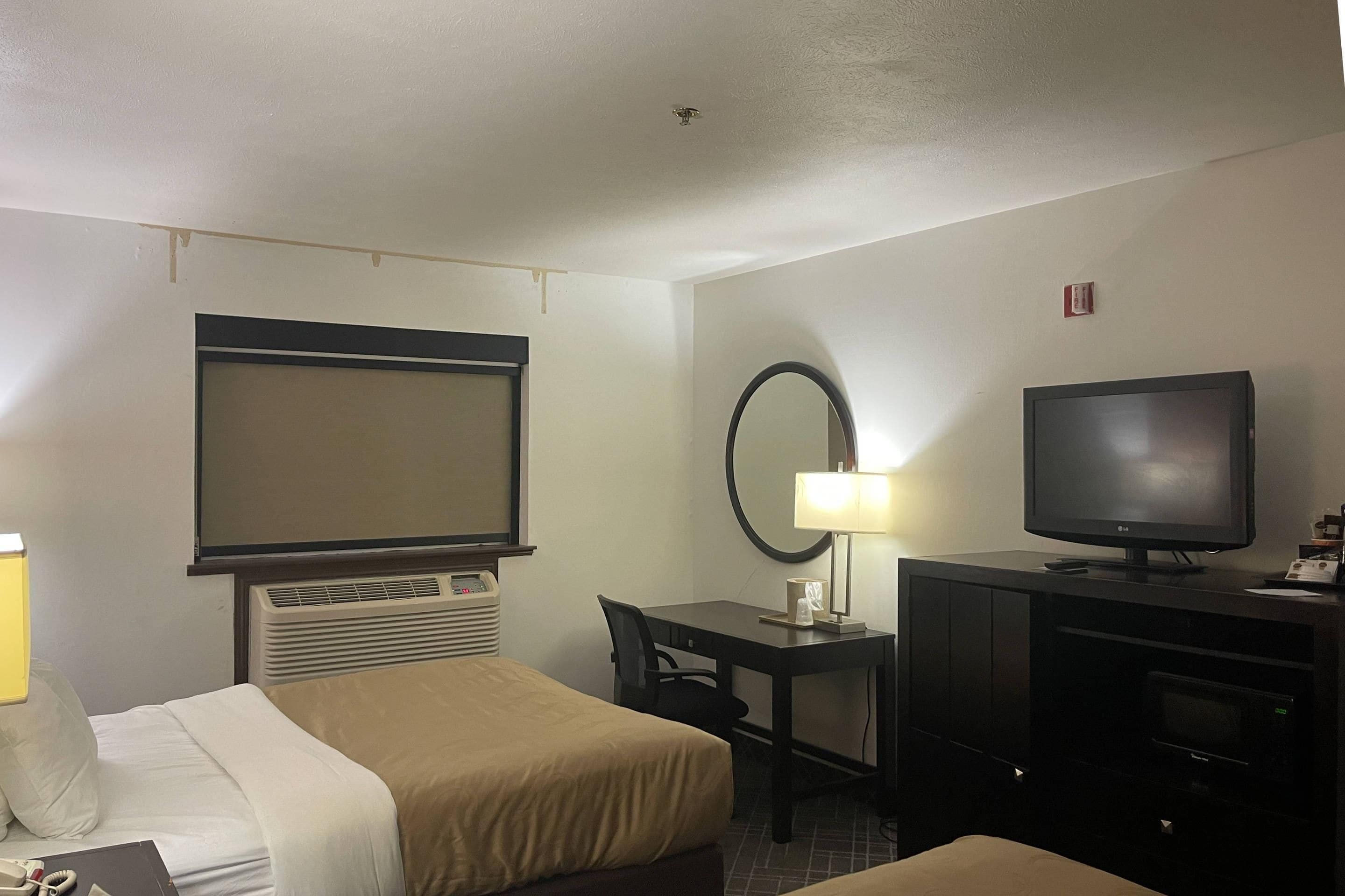 A hotel room with a bed, a desk, a television, and a mirror.