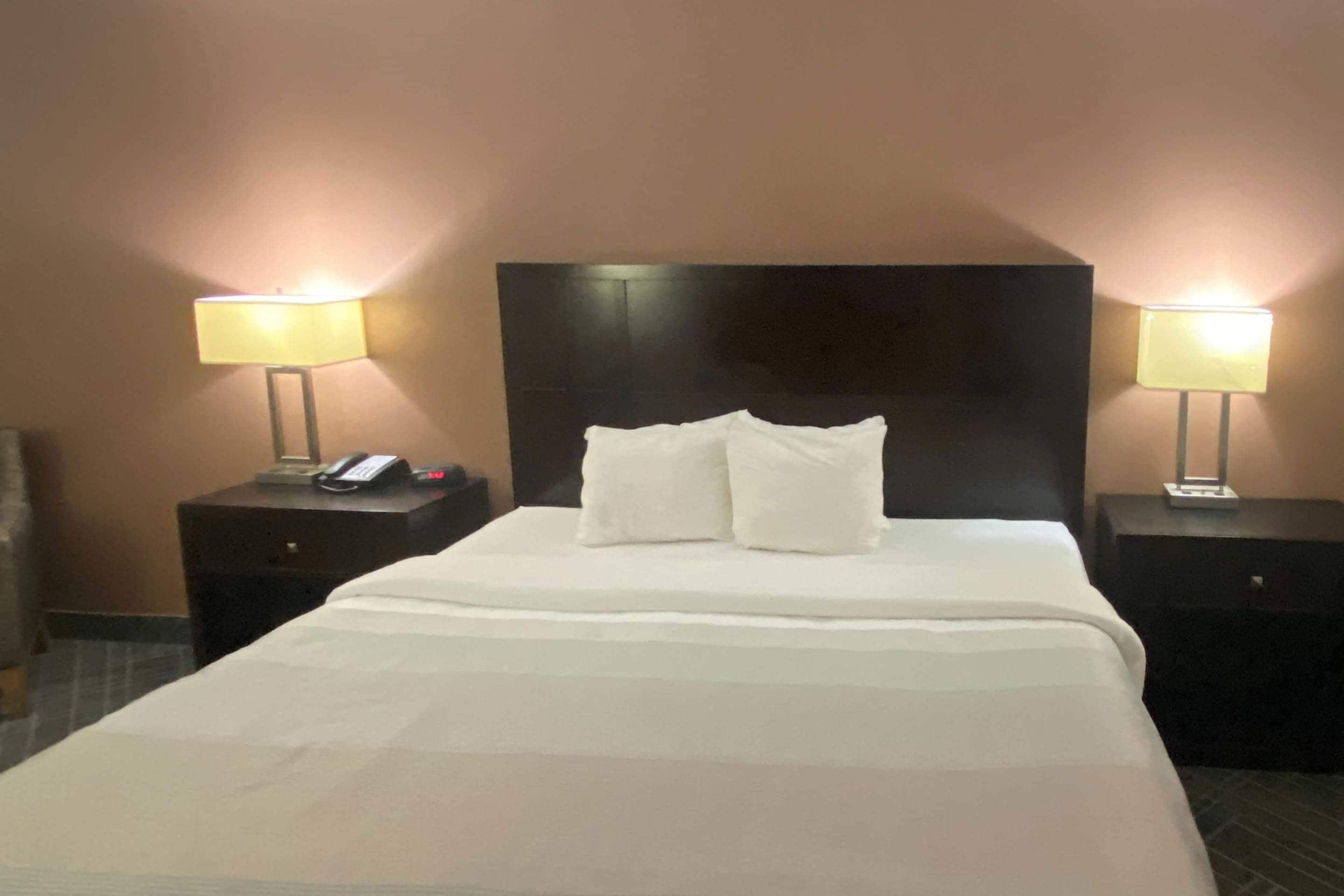 Una habitación de hotel con una cama grande, dos mesitas de noche y dos lámparas.