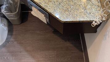 A bathroom with a granite countertop sink, a trash can, and a wooden floor.