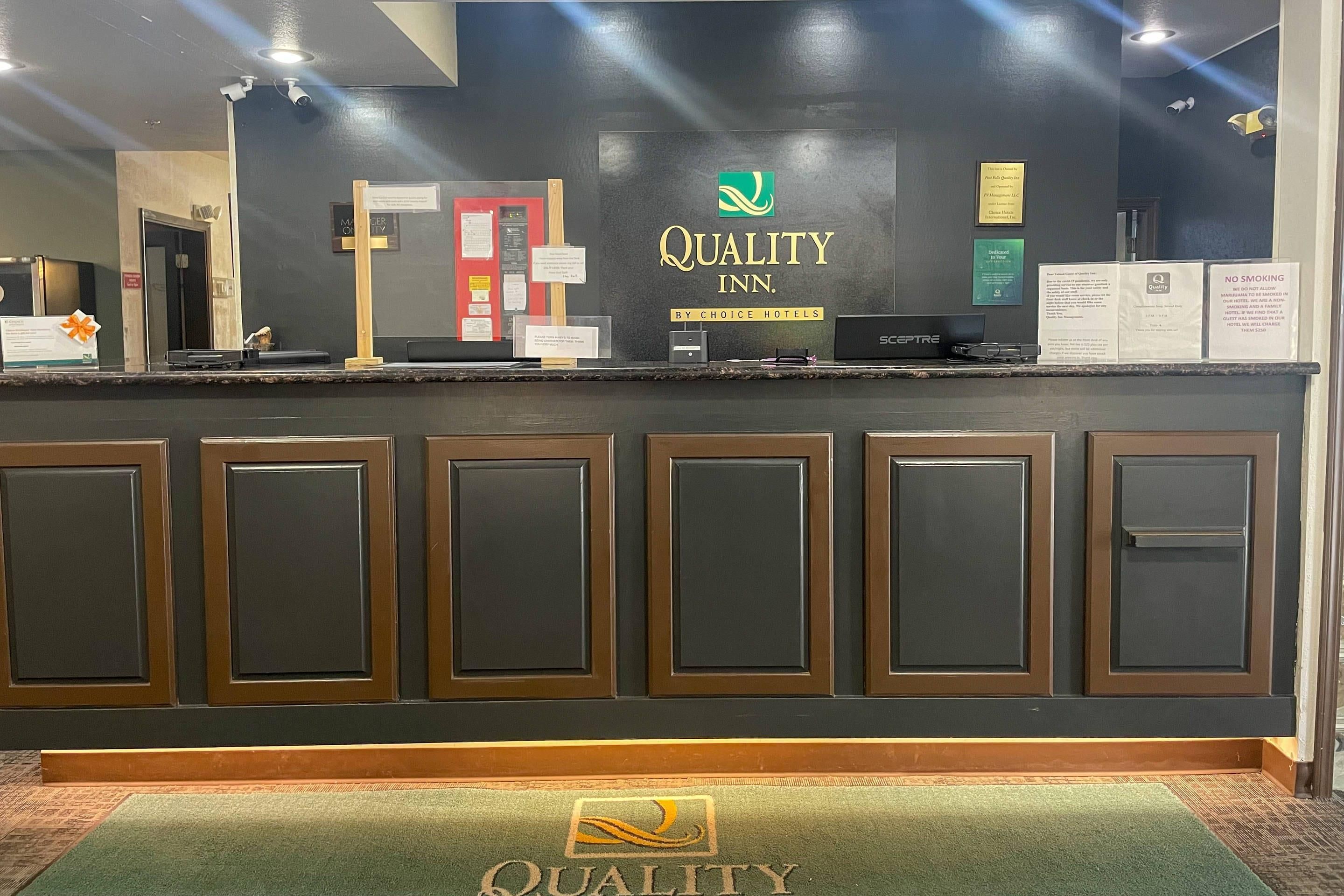 Ein Hotelrezeptionstresen mit einem 'Quality Inn'-Schild, einer Rezeptionstheke und dem 'Quality'-Logo auf der Fußmatte.