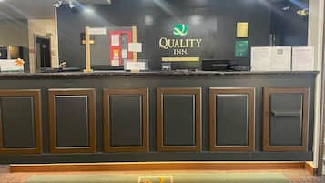 Ein Hotelrezeptionstresen mit einem 'Quality Inn'-Schild, einer Rezeptionstheke und dem 'Quality'-Logo auf der Fußmatte.