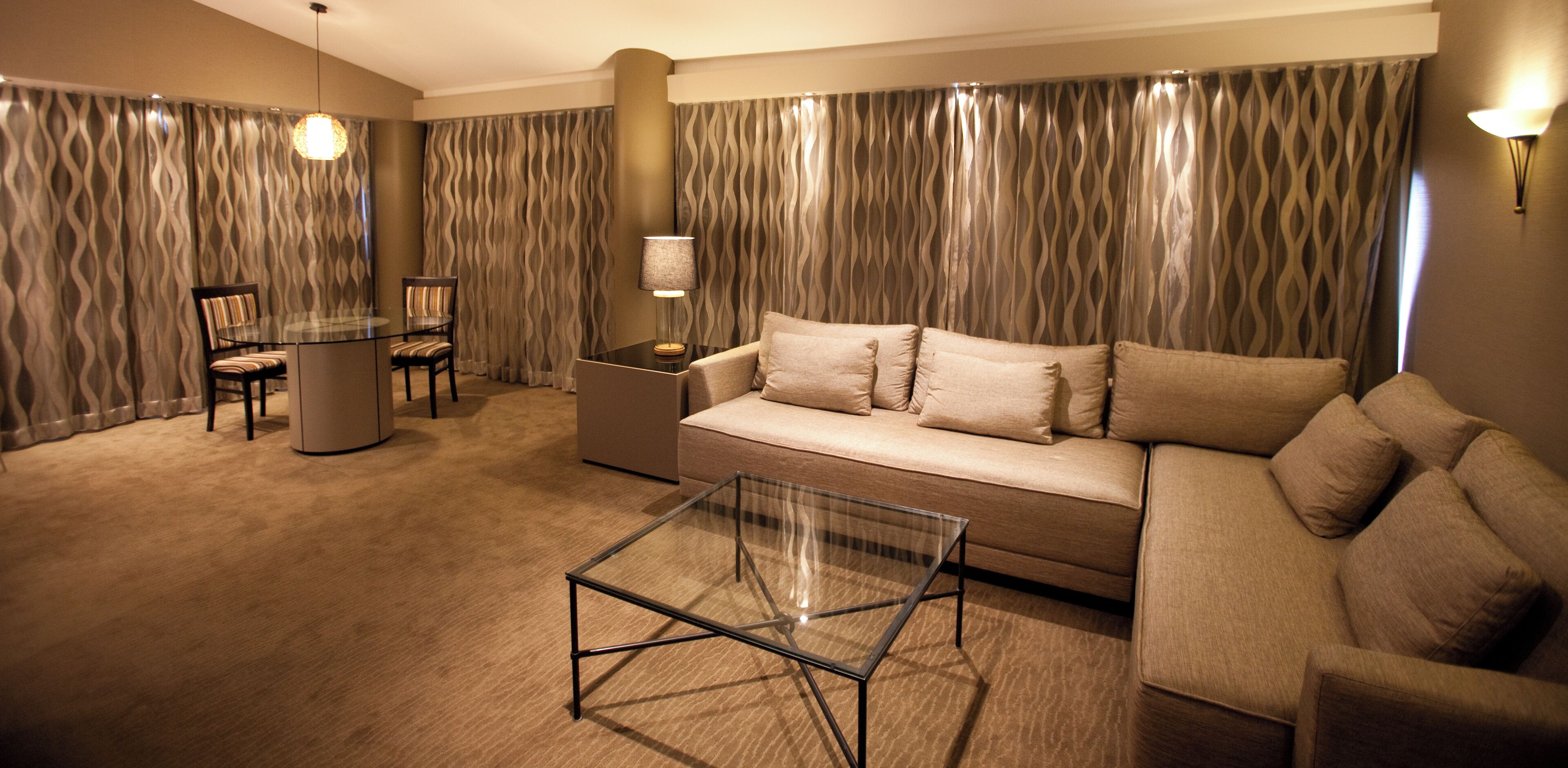 A modern living room with a glass coffee table, a beige sofa, a striped chair, and a lamp.