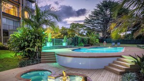 A pool area with a hot tub, wooden deck, and surrounding greenery. - Waipuna Hotel & Conference Centre (Auckland)