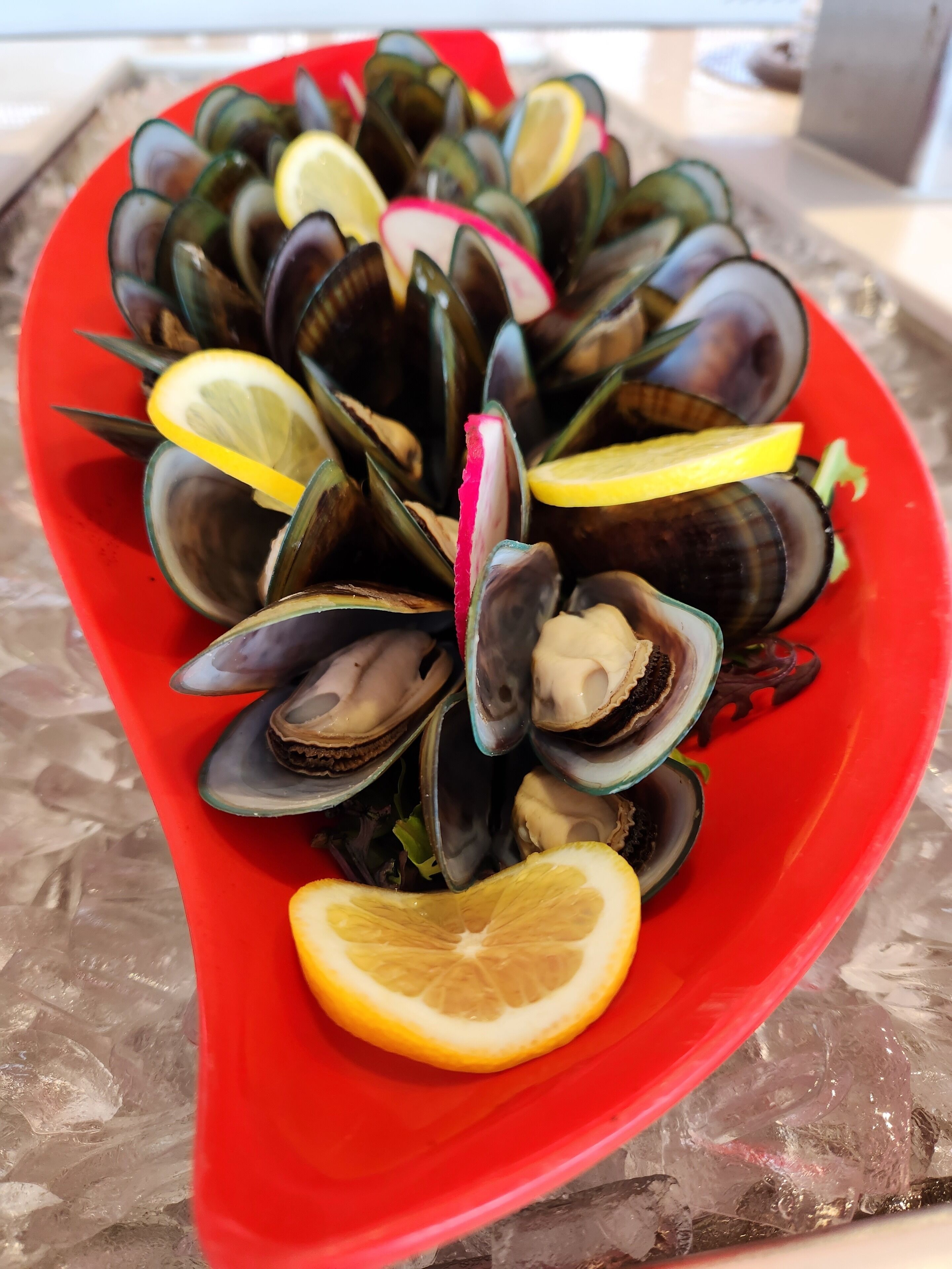 Un plato rojo lleno de mejillones y rodajas de limón.