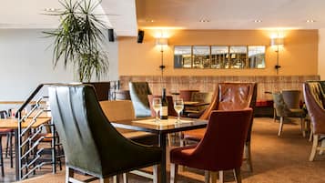 A hotel lobby with a dining area featuring leather chairs, a potted plant, and a large mirror on the wall.