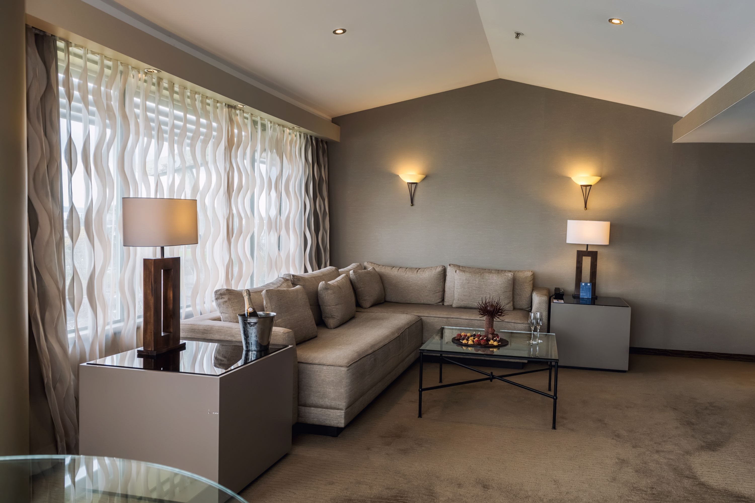 A modern living room with a sectional sofa, a glass coffee table, and two wall-mounted lamps.