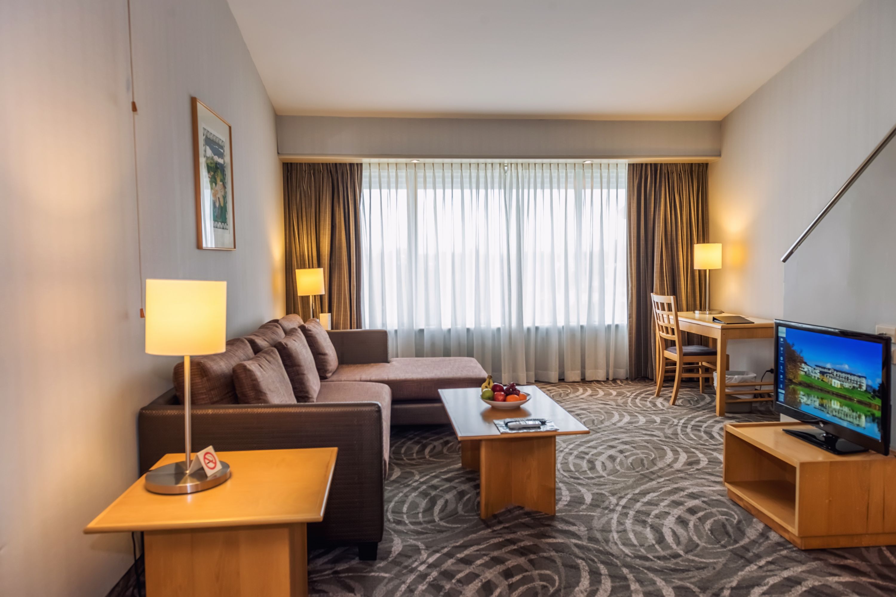 A hotel room with a sofa, two armchairs, a coffee table, a TV, and a desk with a chair.