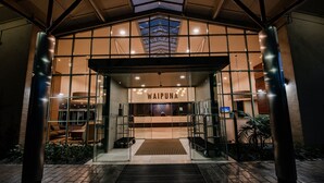 The entrance to a hotel with a modern design, featuring glass doors, a reception desk, and a visible seating area inside. - Waipuna Hotel & Conference Centre (Auckland)