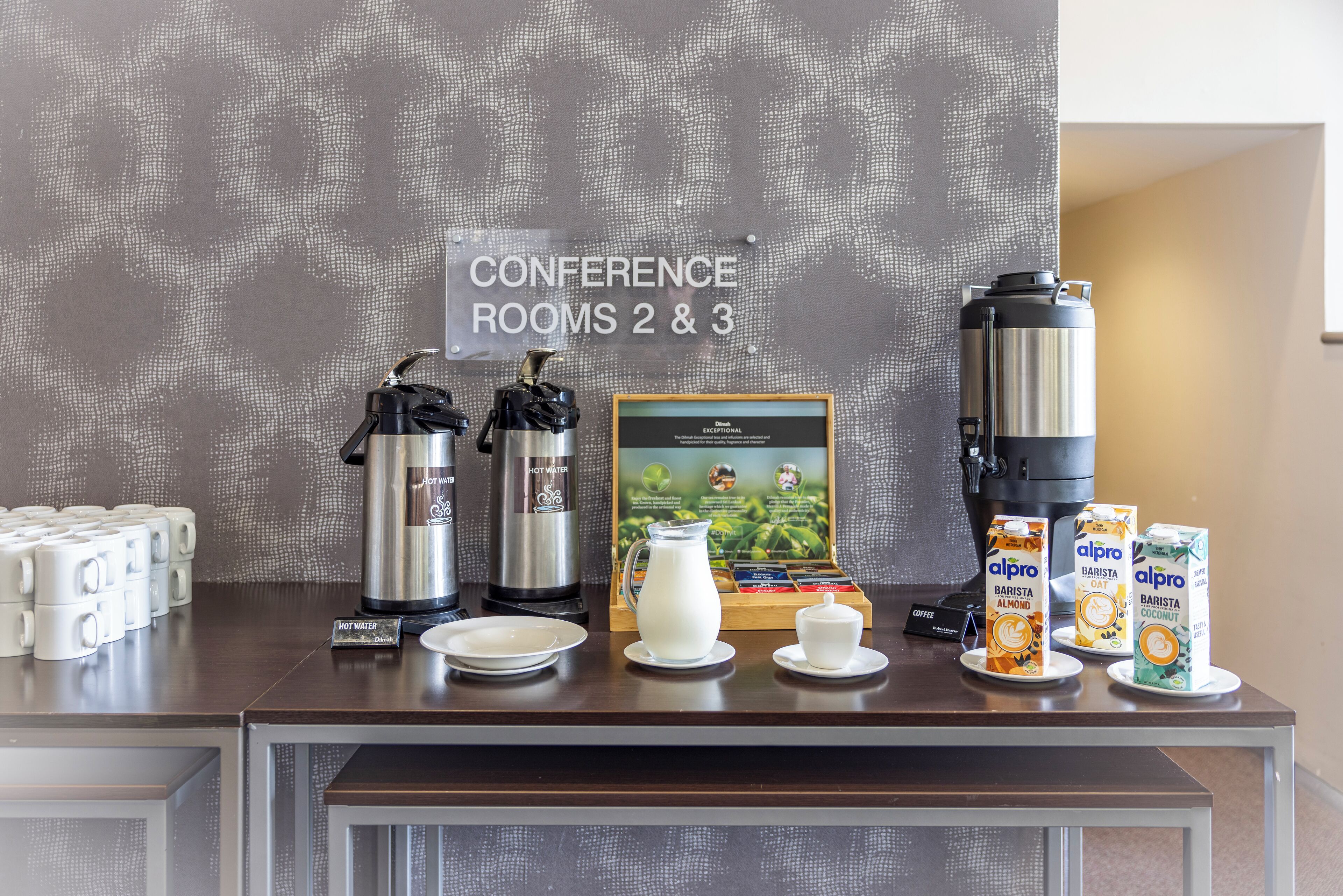 Una mesa con cafeteras, un jarro y bebidas Alpro barista.