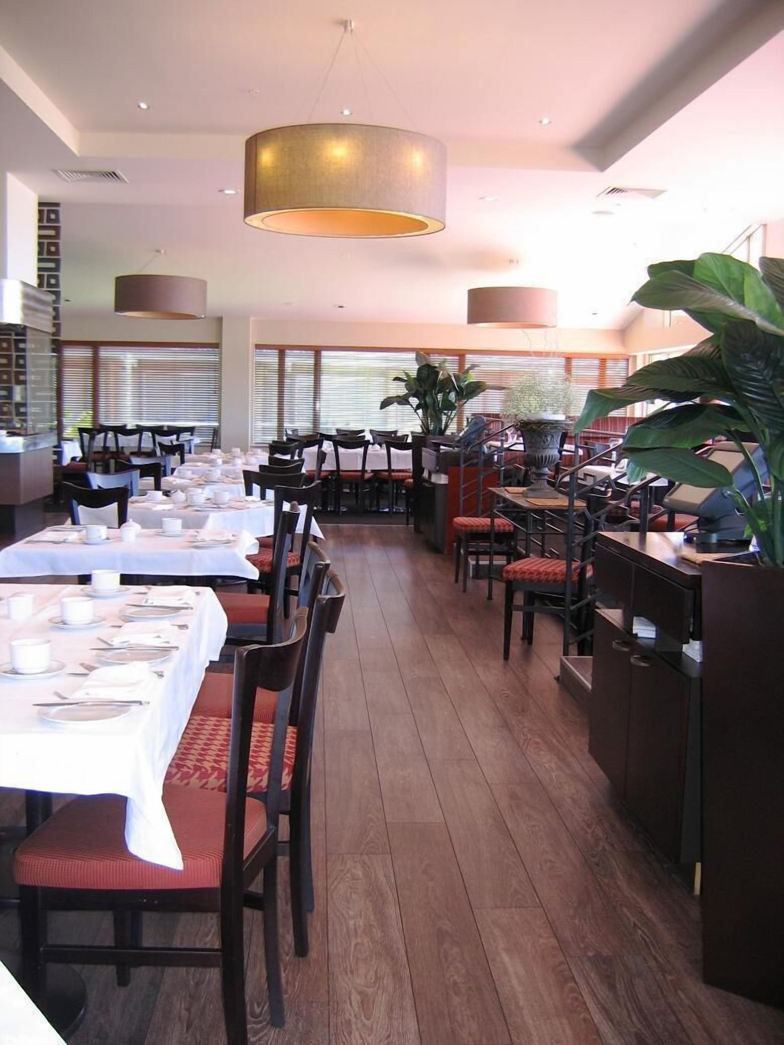 A restaurant with multiple dining tables set for service, large potted plants, and a modern interior design.
