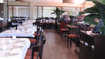 Un restaurante con varias mesas dispuestas para recibir comensales, grandes macetas y una decoración de estilo moderno.