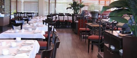 Un restaurante con varias mesas dispuestas para recibir comensales, grandes macetas y una decoración de estilo moderno.