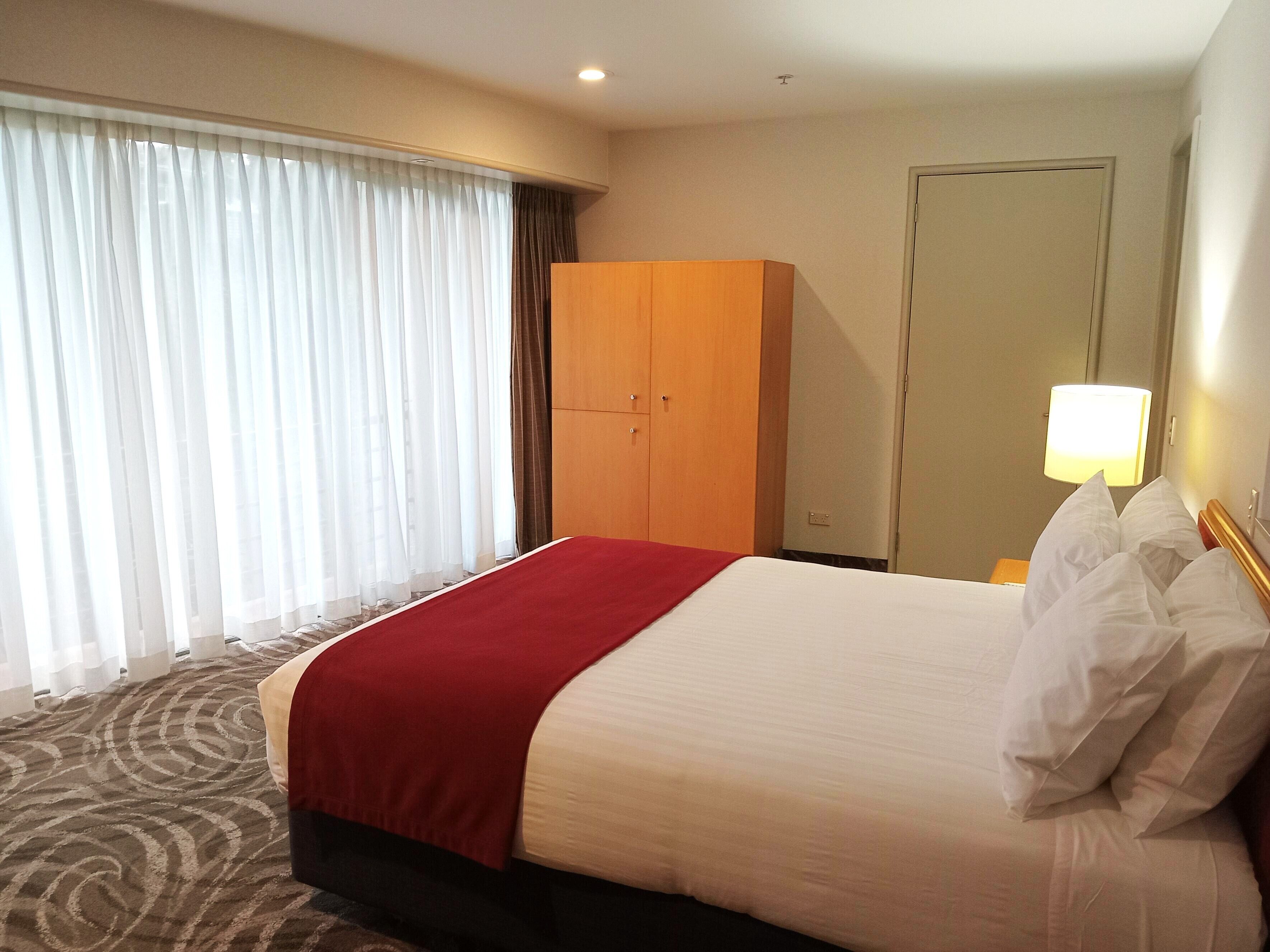 A hotel room with a bed, a wardrobe, a door, and a window with curtains.