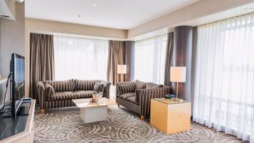 A hotel room with a large sofa set, a coffee table, a TV, and a desk with a lamp.