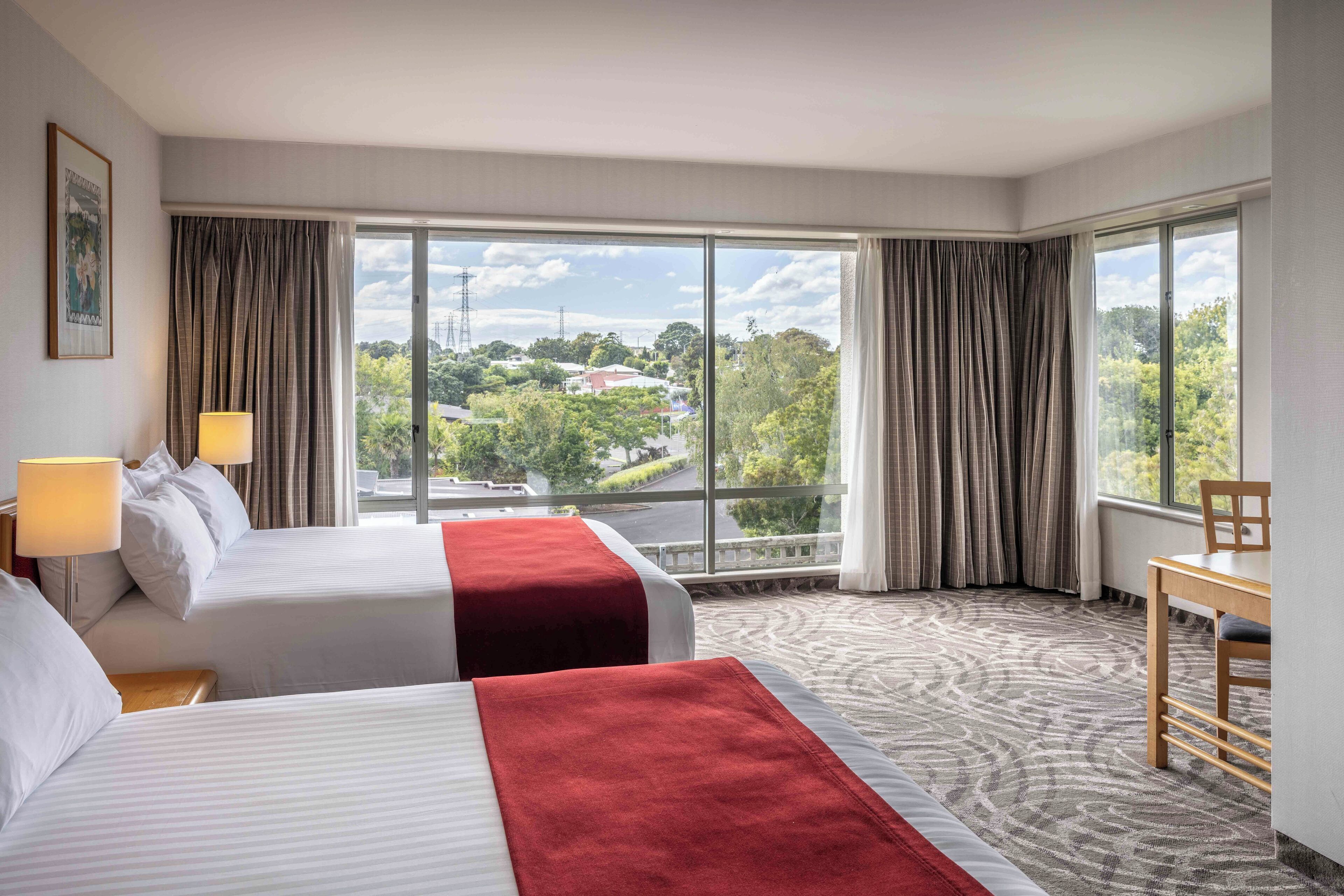 A hotel room with two beds, a view of the city, and a dining area.