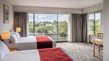 A hotel room with two beds, a view of the city, and a dining area.