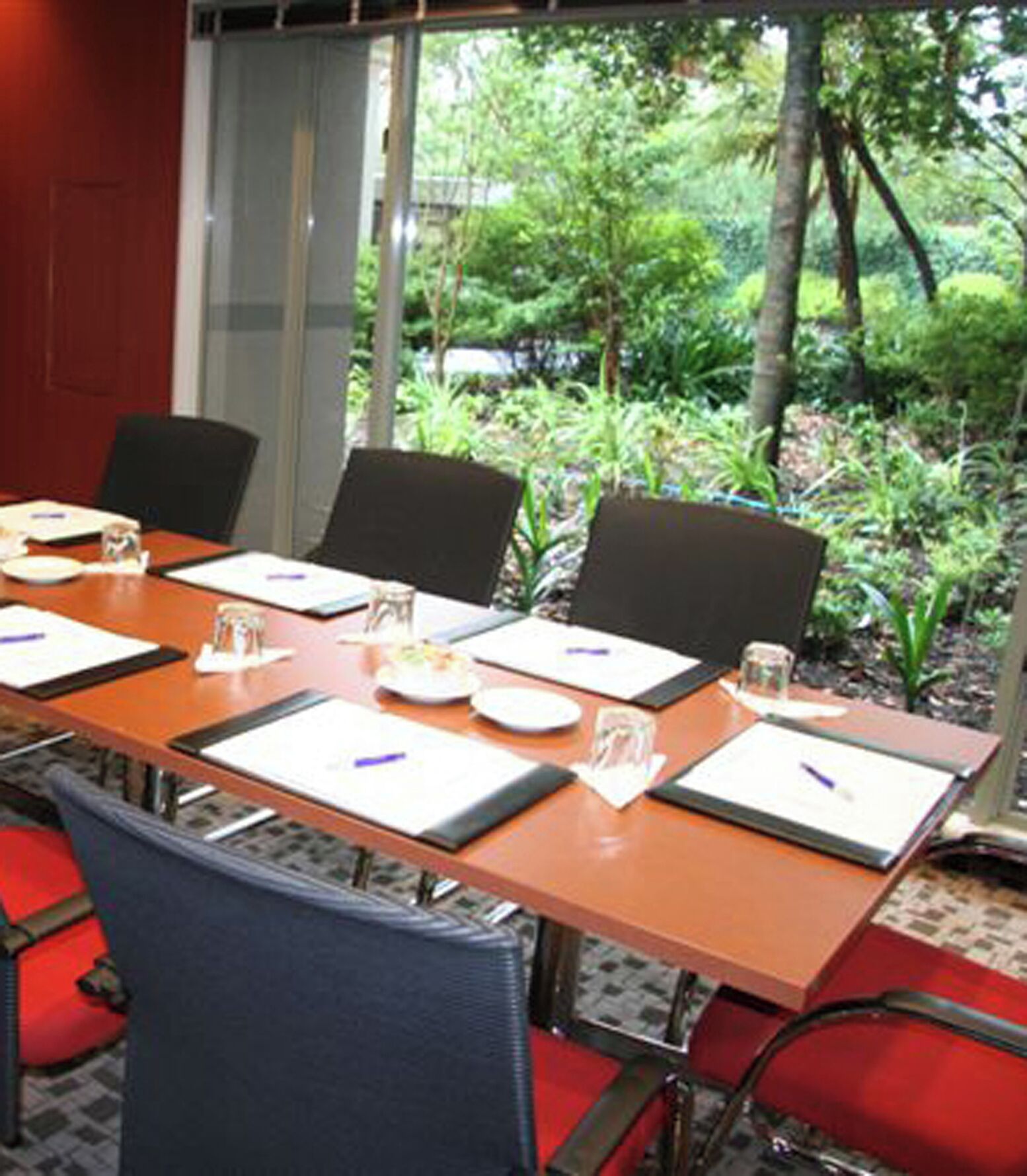 A conference room with a long table, chairs, and a view of greenery outside.