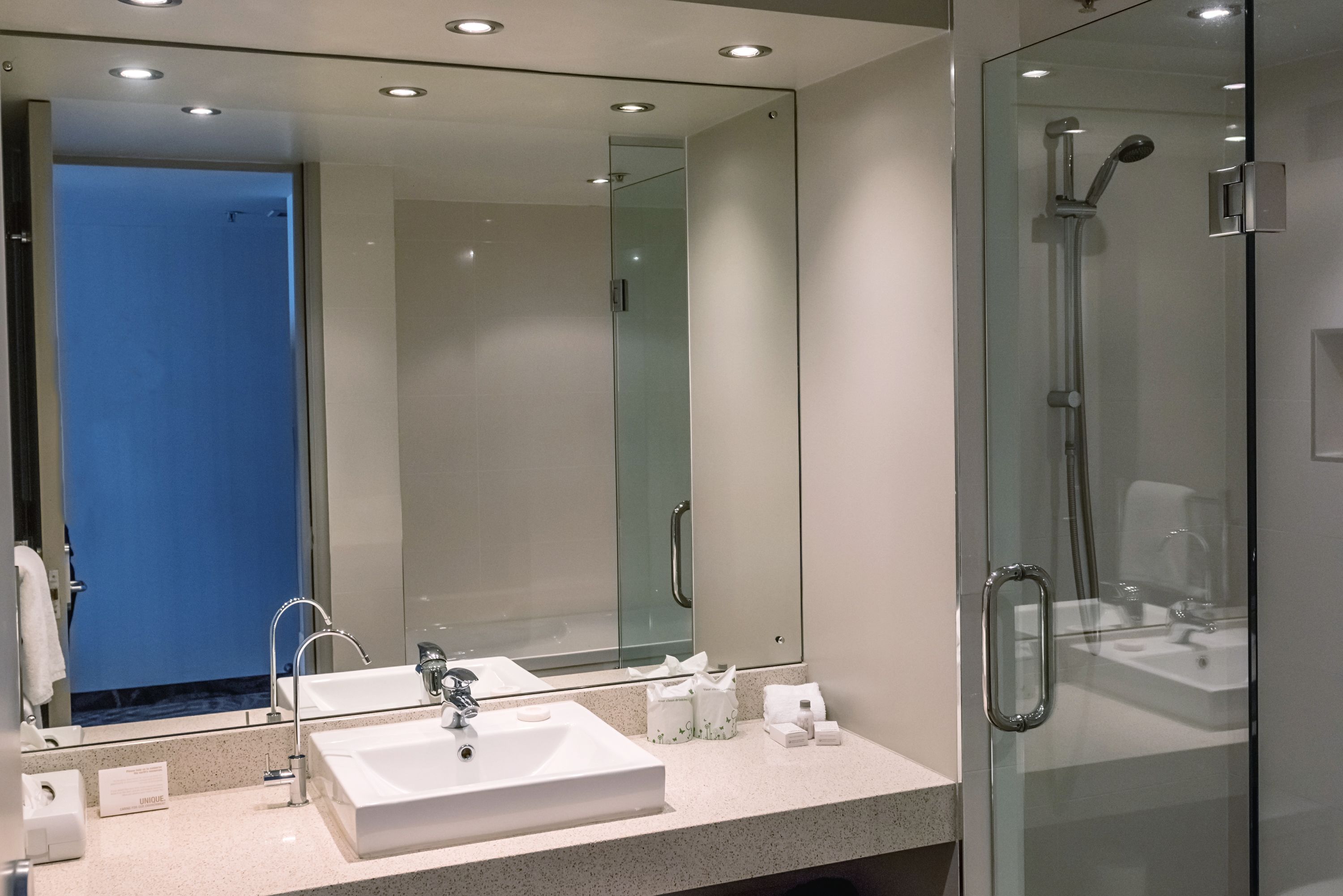 A modern bathroom with a large mirror, two sinks, a shower, and a glass-enclosed shower area.