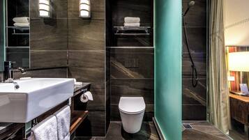 Een moderne badkamer met een wit wastafel, toilet en douche. Handdoekrekken en een plank met toiletartikelen.