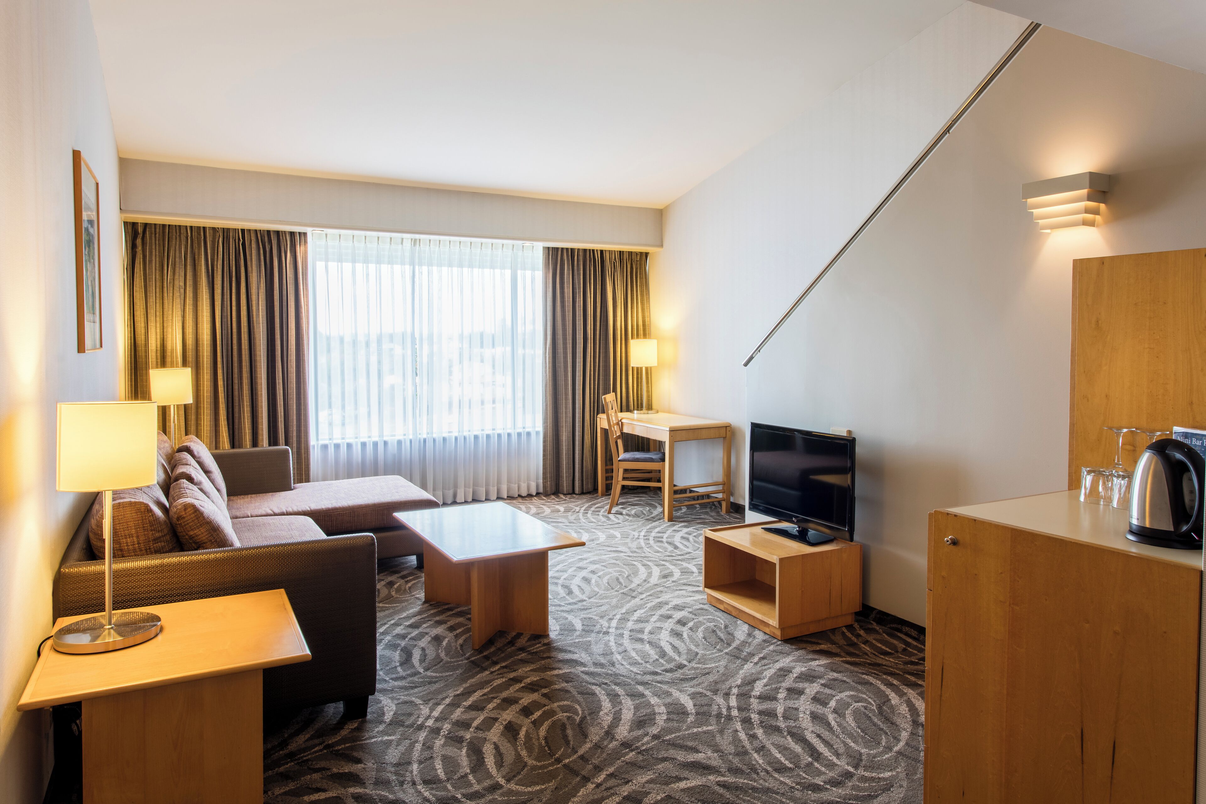 Una habitación de hotel con sofá, una mesita, televisor y armario.