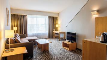 Una habitación de hotel con sofá, una mesita, televisor y armario.