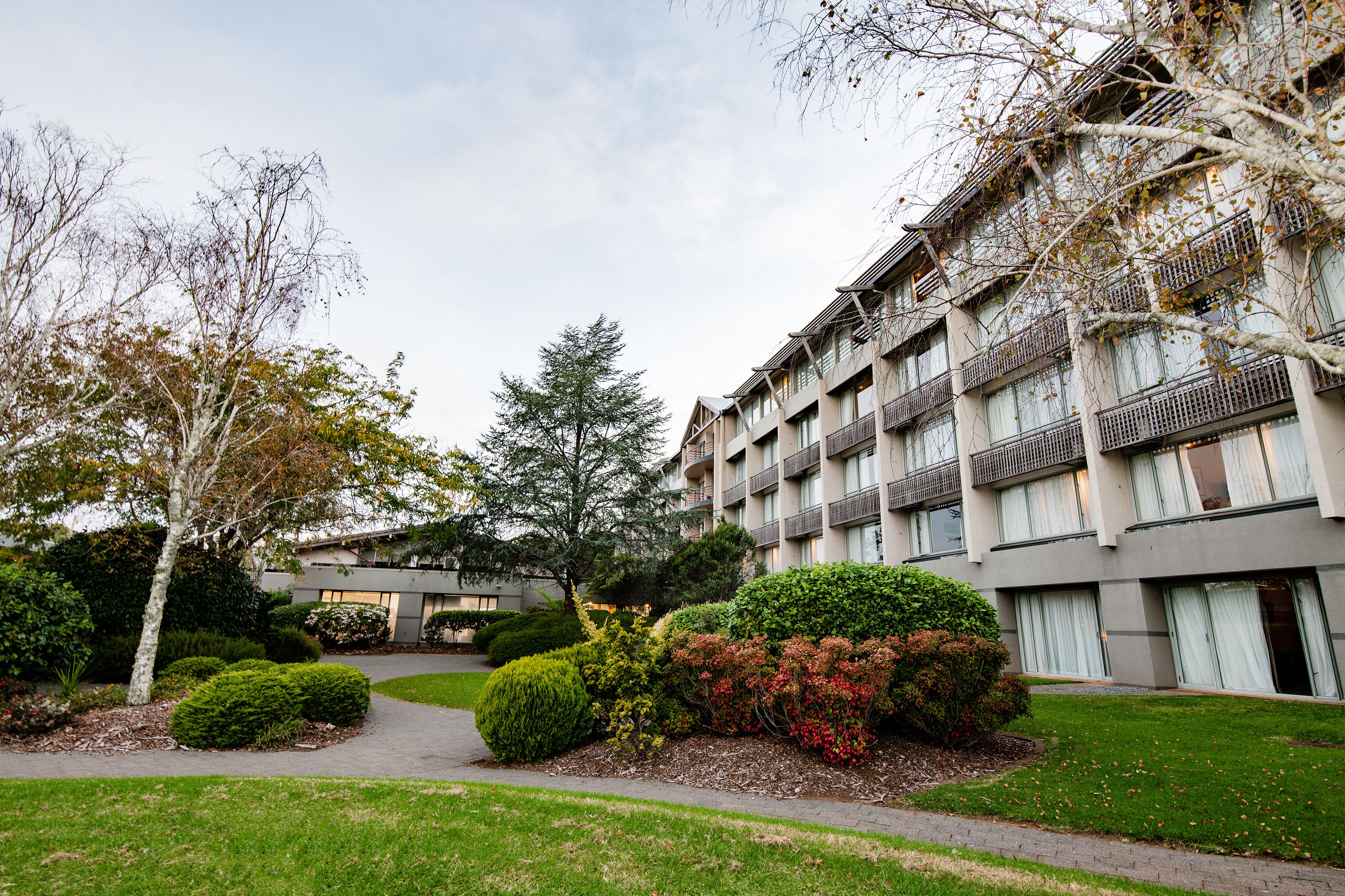 A multi-story building with balconies, surrounded by well-maintained lawns and various shrubs.