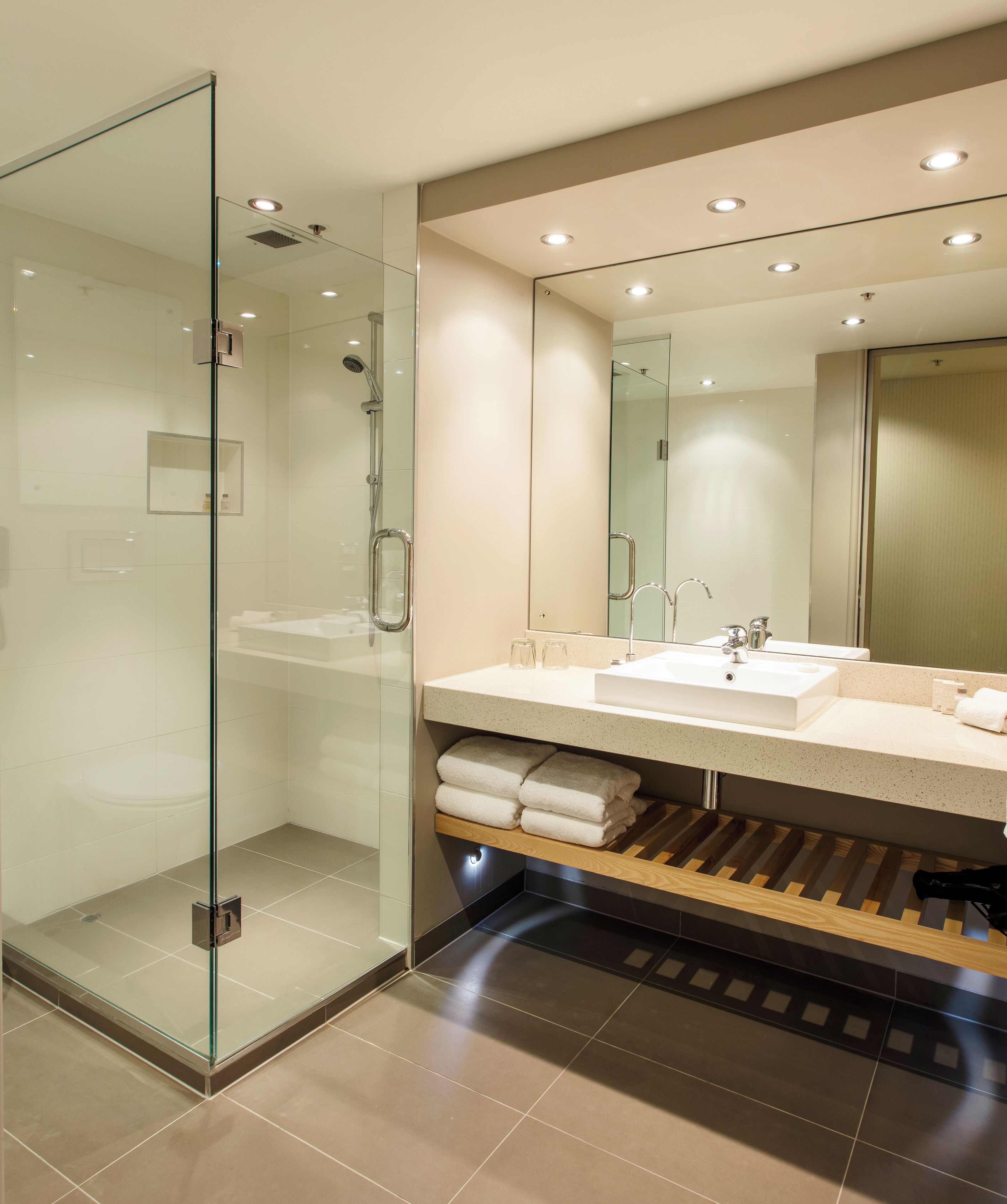 Une salle de bain moderne dotée d’une douche à parois de verre, d’un grand miroir et d’un meuble-lavabo à deux vasques.