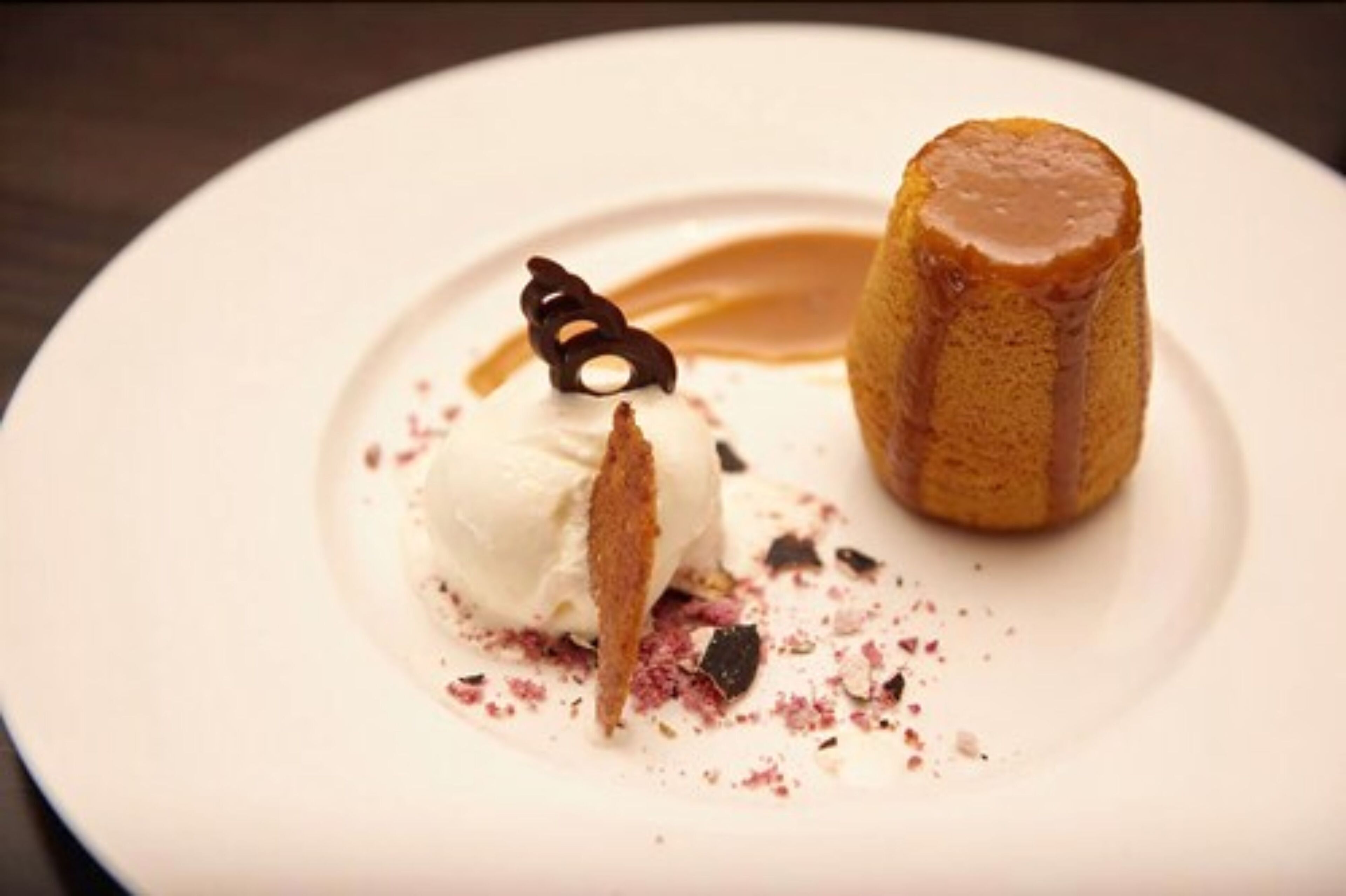 Een nagerechtbord met een caramelpudding en een bol ijs.