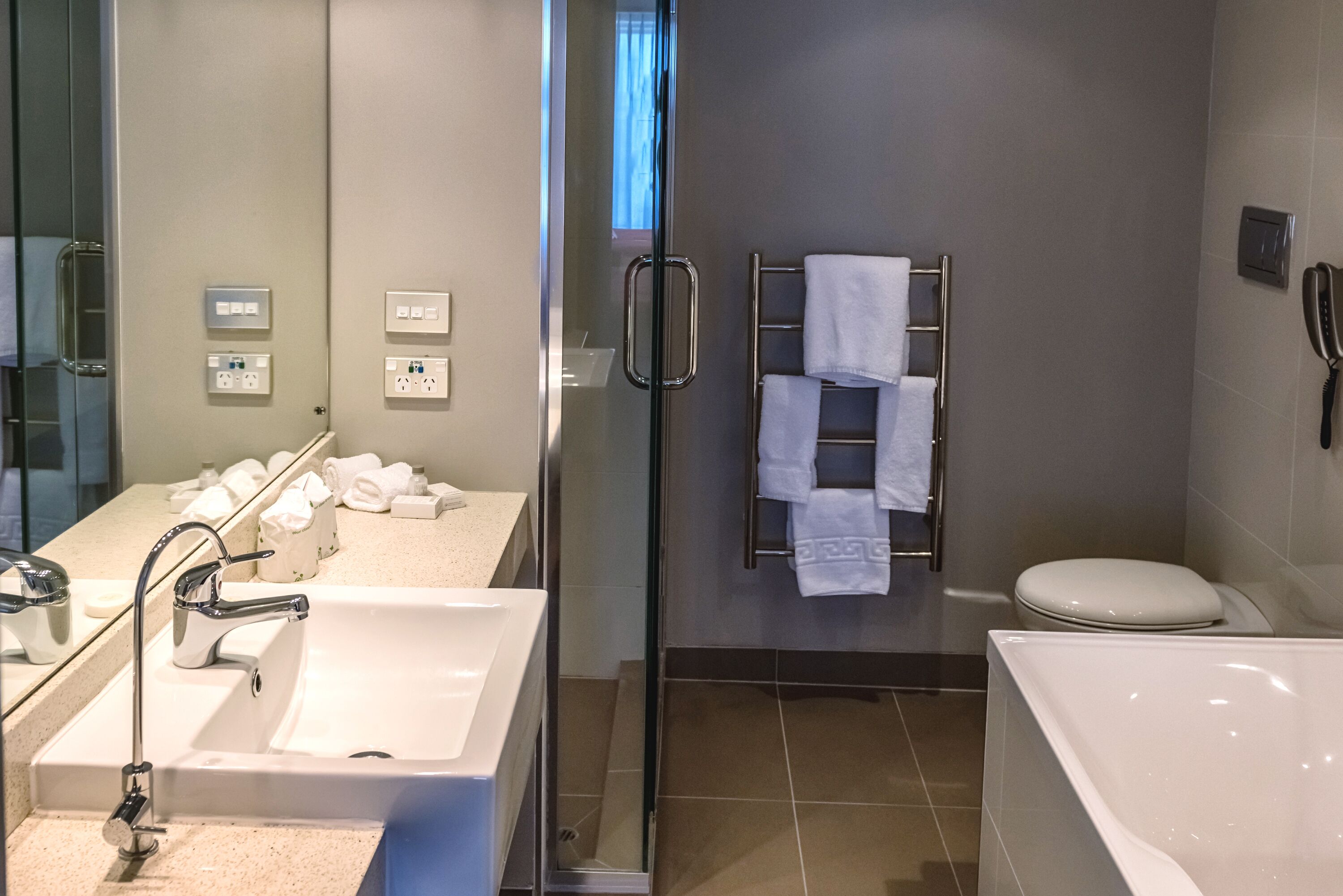 A modern bathroom with a glass shower enclosure, a white sink, a bathtub, and a towel rack with multiple towels.