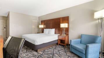 A hotel room with a bed, bedside tables with lamps, a blue armchair, and a patterned carpet.