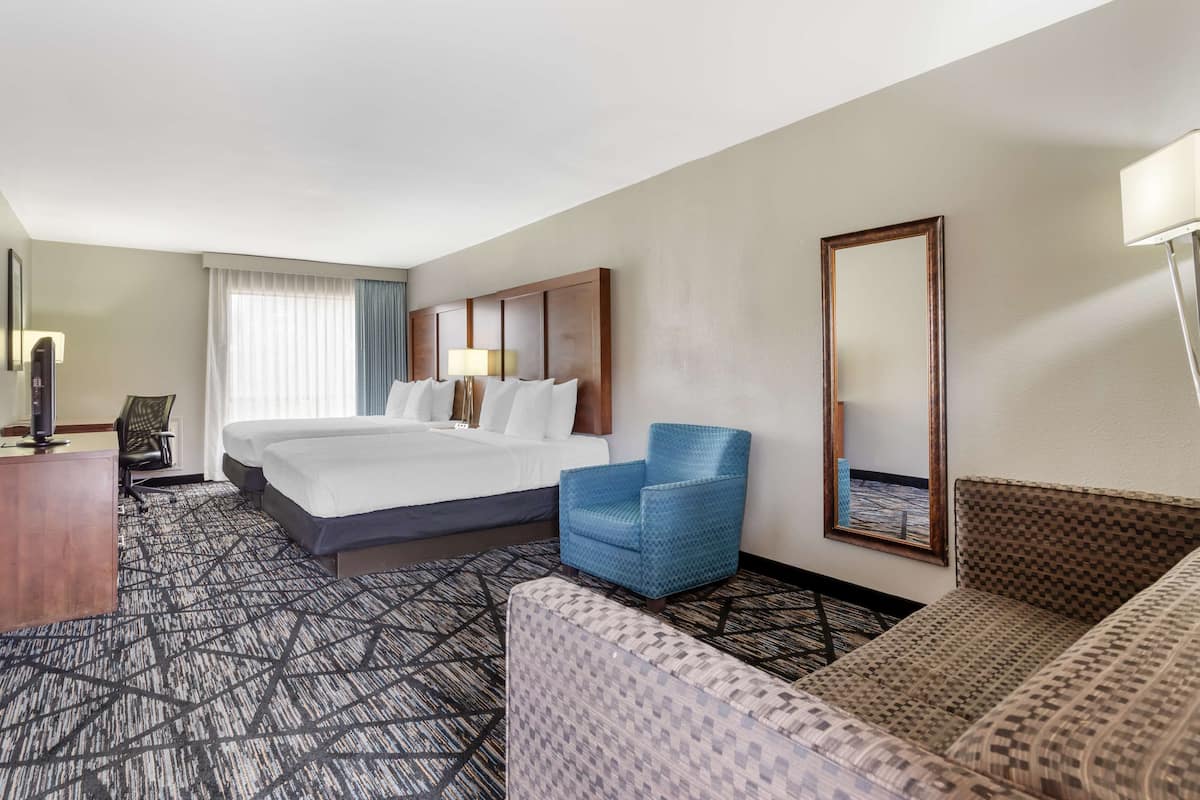 A hotel room with a large bed, a blue armchair, a patterned sofa, a desk, and a large mirror.