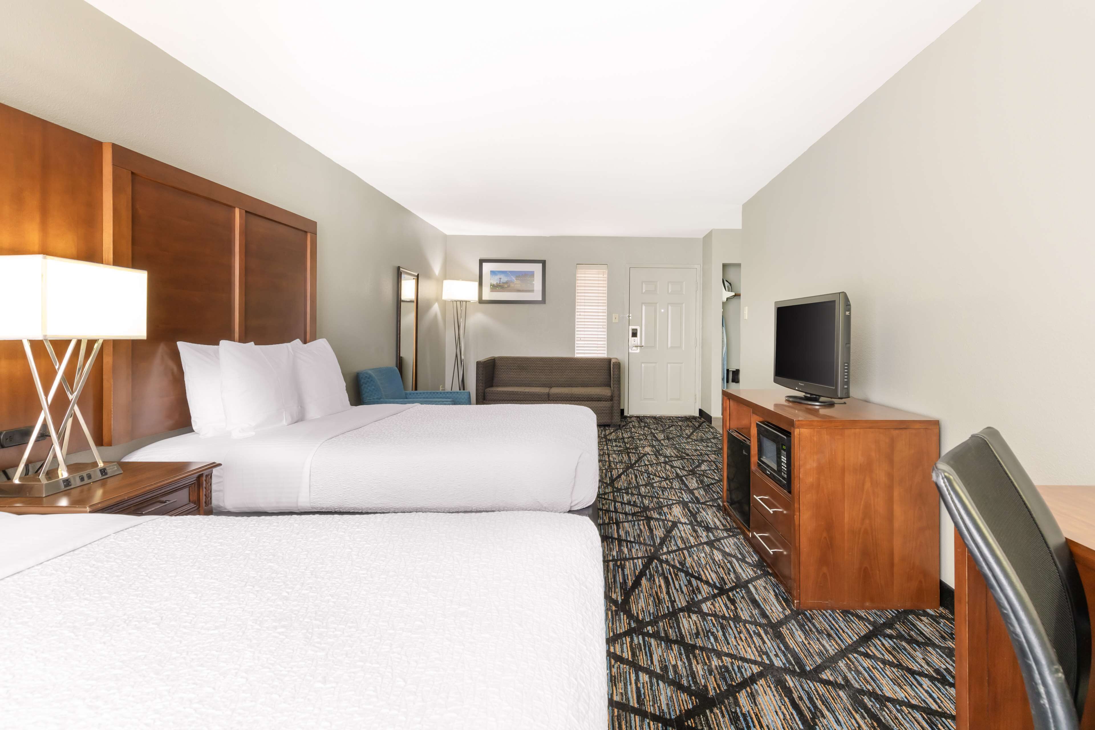 Quarto de hotel com duas camas, uma escrivaninha com televisão, um abajur e um tapete estampado.