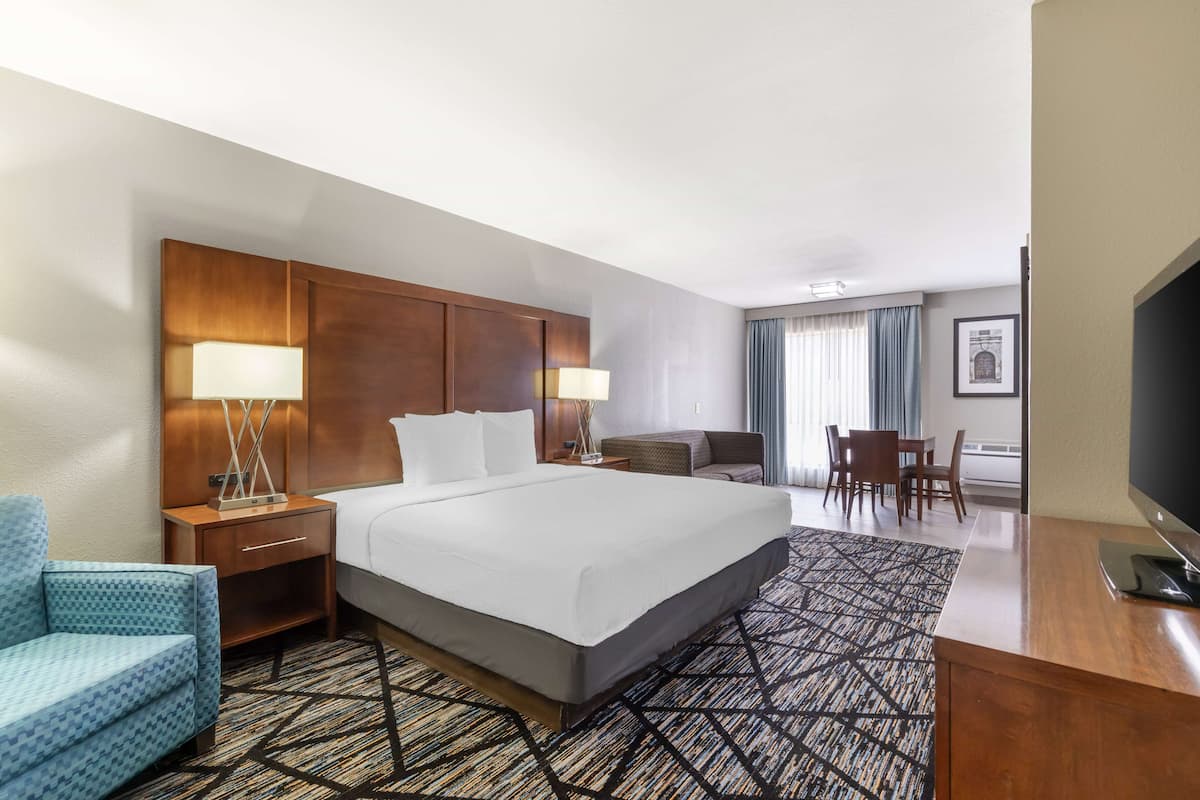 A hotel room with a large bed, a desk, a chair, a TV, and a lamp.