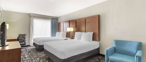 A hotel room with two beds, a desk, a TV, and a blue armchair.