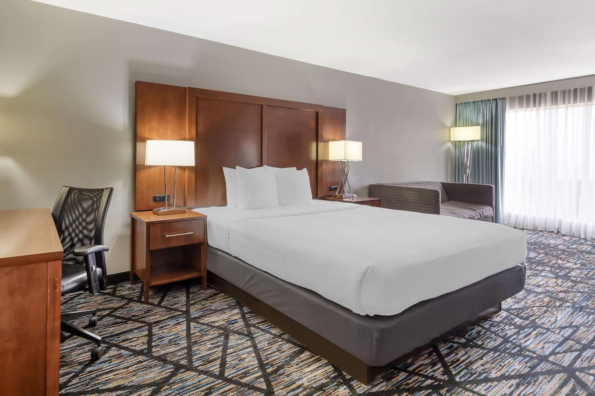A hotel room with a large bed, two bedside tables with lamps, a desk, a chair, and a patterned carpet.