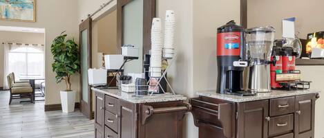 A breakfast bar with coffee makers and a sign indicating breakfast hours.