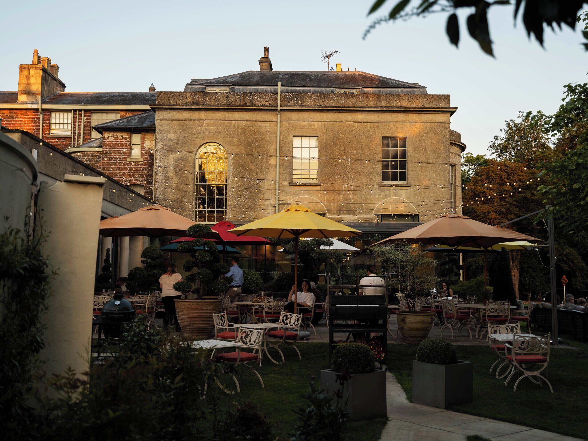 An outdoor patio area with tables and chairs, surrounded by a brick building with arched windows and a clock tower.
