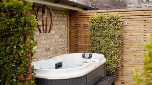 A hot tub in a garden with a stone wall, wooden fence, and lush greenery. - Bishopstrow Hotel & Spa (Warminster)