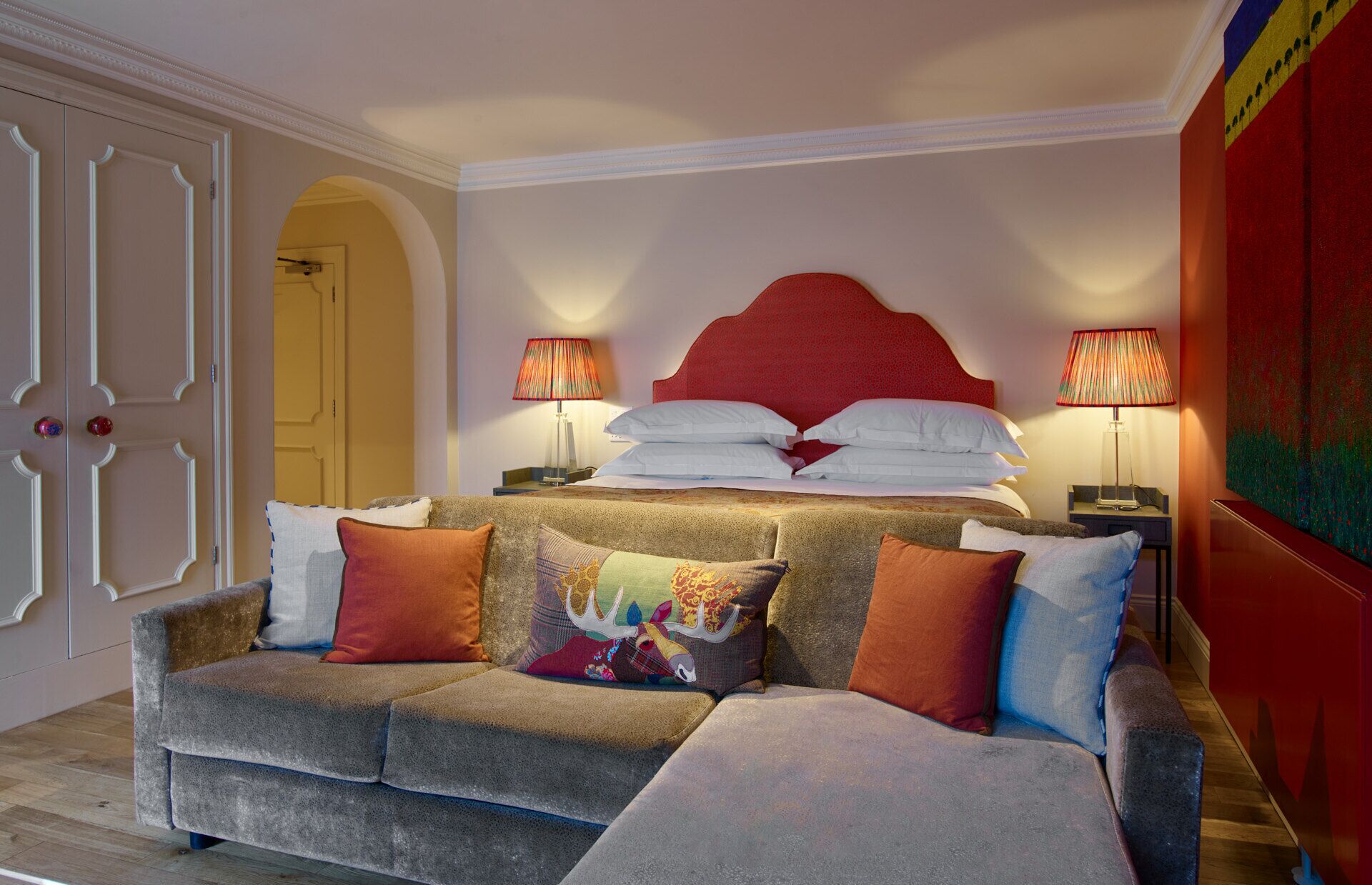 A bedroom with a bed, a sofa, two lamps, and a door.