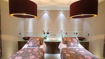 A room with two beds, a sink, and a mirror. There are two large lamps hanging from the ceiling.