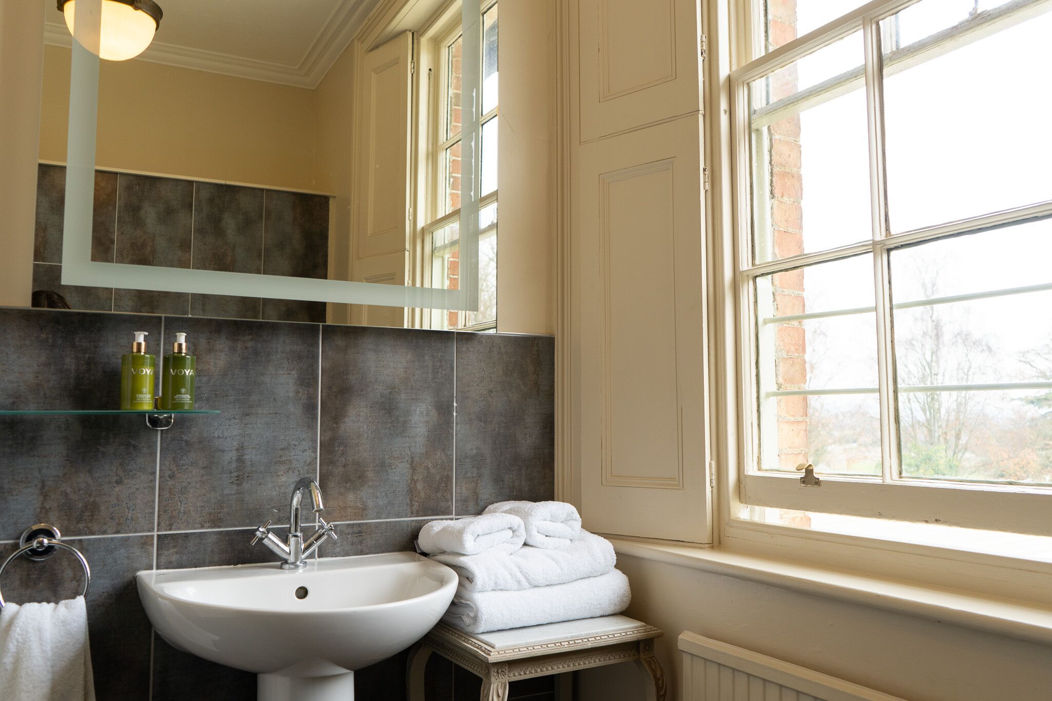 A bathroom with a white sink, a mirror, and a window.