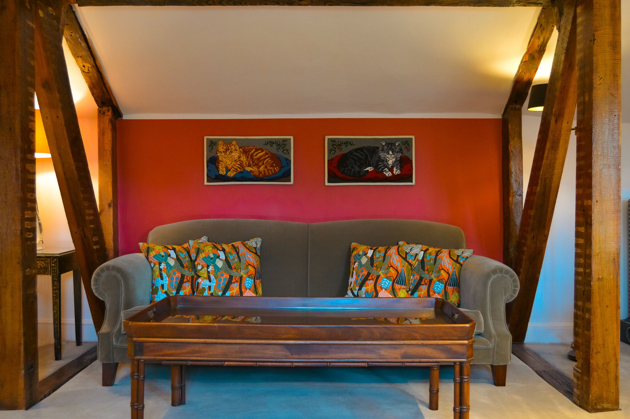 A cozy living room with a grey sofa, colorful patterned pillows, and two framed animal paintings on the wall.