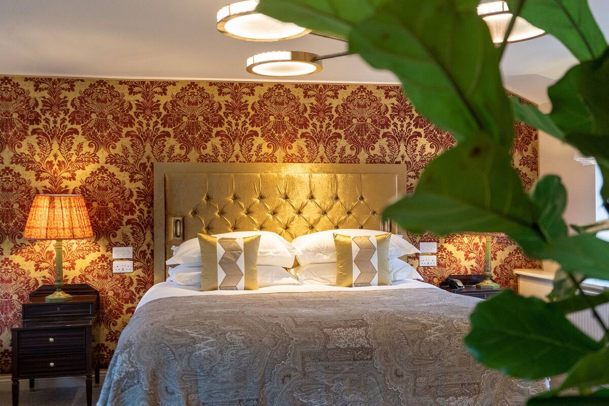 A hotel room with a tufted headboard, a patterned wall, a bedside lamp, and a nightstand.