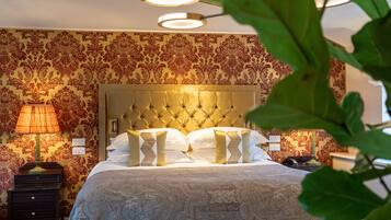 Una habitación de hotel con cabecera capitonada, pared con estampado, lámpara de noche y mesita de noche.