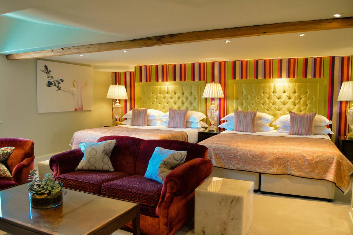A hotel room with two beds, a red velvet sofa, and a small table with a plant.