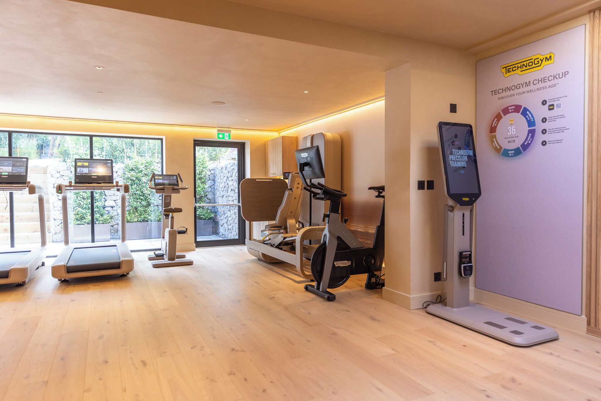 Un gimnasio con máquinas de cardio, una bicicleta estática y una pantalla digital en la pared.