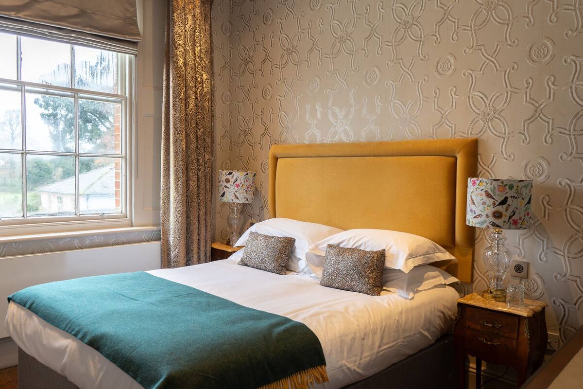 A neatly made bed with a green blanket, two pillows, and a wooden nightstand with a lamp.
