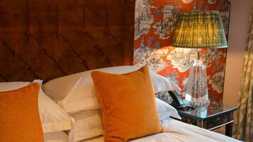 A hotel room with a tufted headboard, a bed with white linens and orange pillows, a nightstand with a lamp, and a wall with a traditional landscape painting.